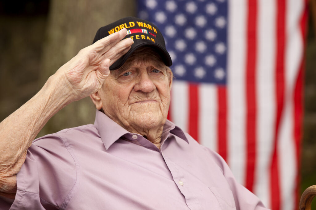 Male veteran wearing a World War II hat saluting